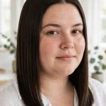 A woman with a round face and a sleek, centre-parted lob in dark brown hair falling past her chin, standing in a bright room with soft daylight, shown from the shoulders up, wearing a white shirt, with the long vertical lines of the cut elongating her face.
