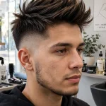 A young adult man with a burst fade and layered mohawk crown, standing in a bright modern barbershop, front three-quarter view, natural daylight, clean bright style, sharp focus on the curved fade.