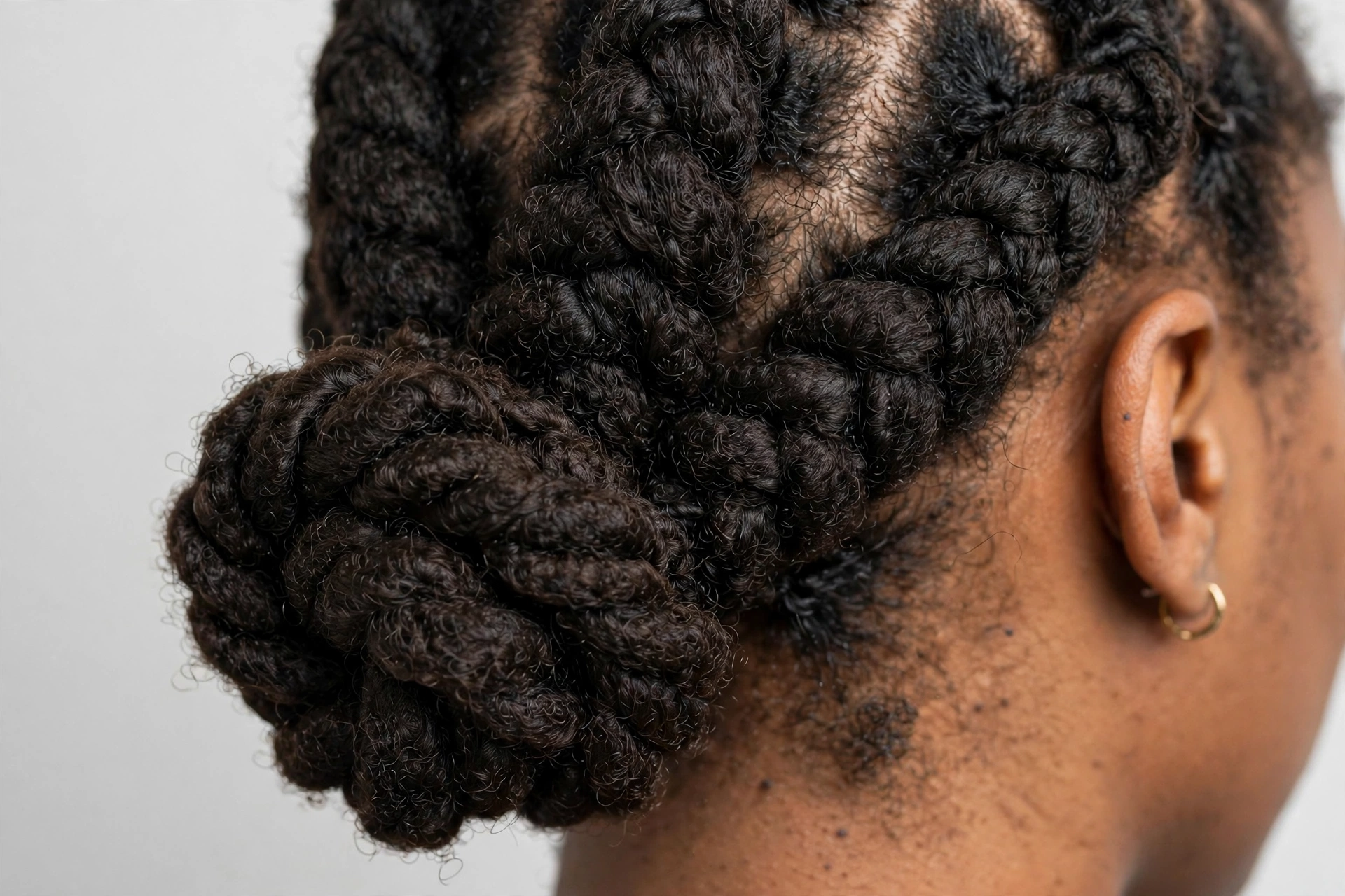 Close-up of chunky flat twists gathered into a low bun, photographed in a bright studio with a neutral background.