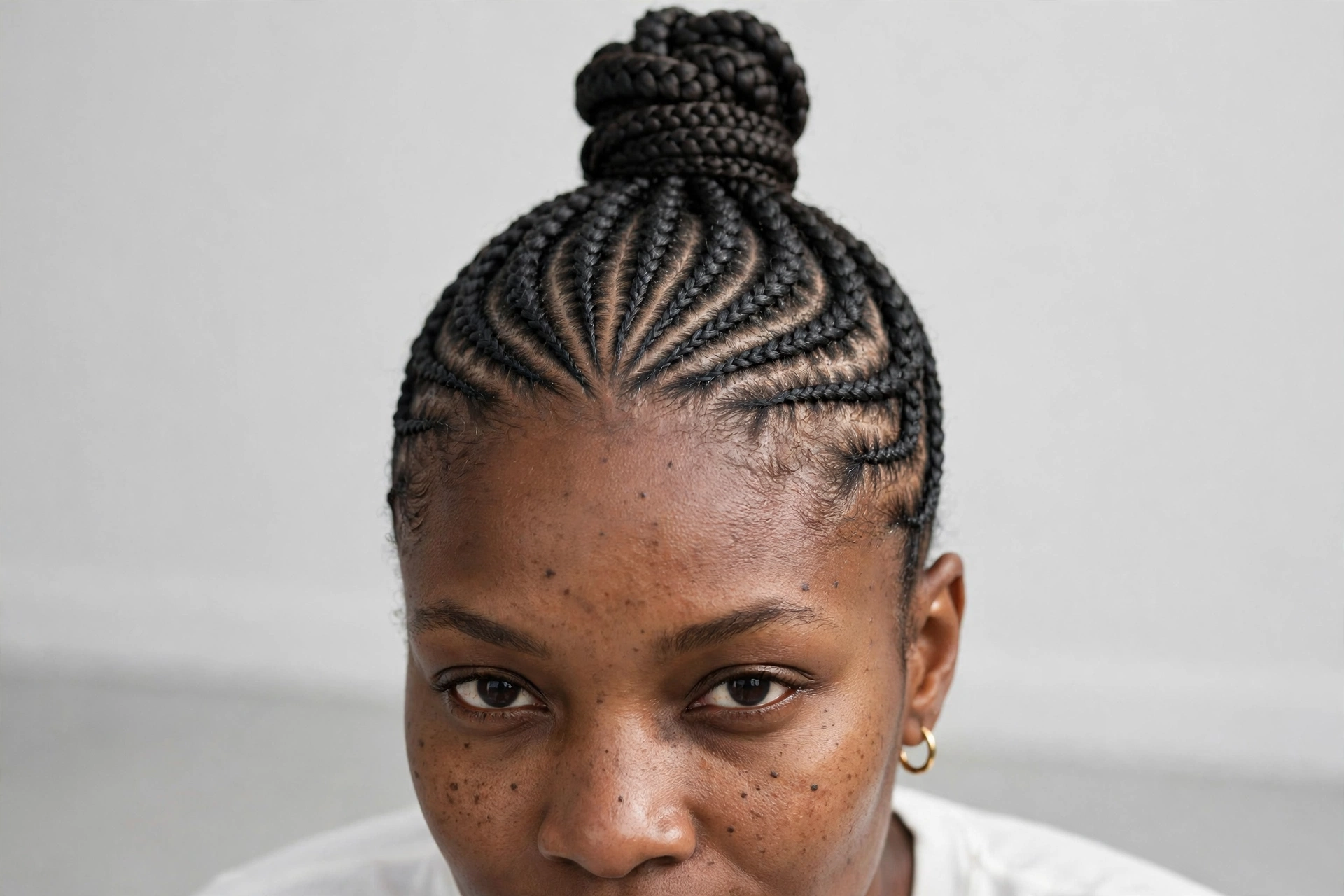 Close-up of cornrows gathered into a sleek high bun, photographed in a bright studio with a neutral background.